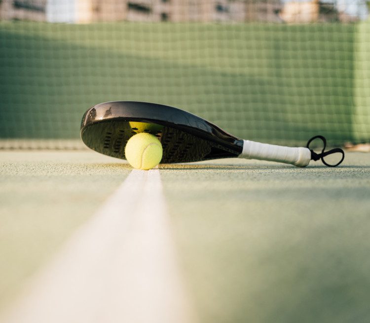 Paddle tennis racquet and padel ball on a green court in the sunset